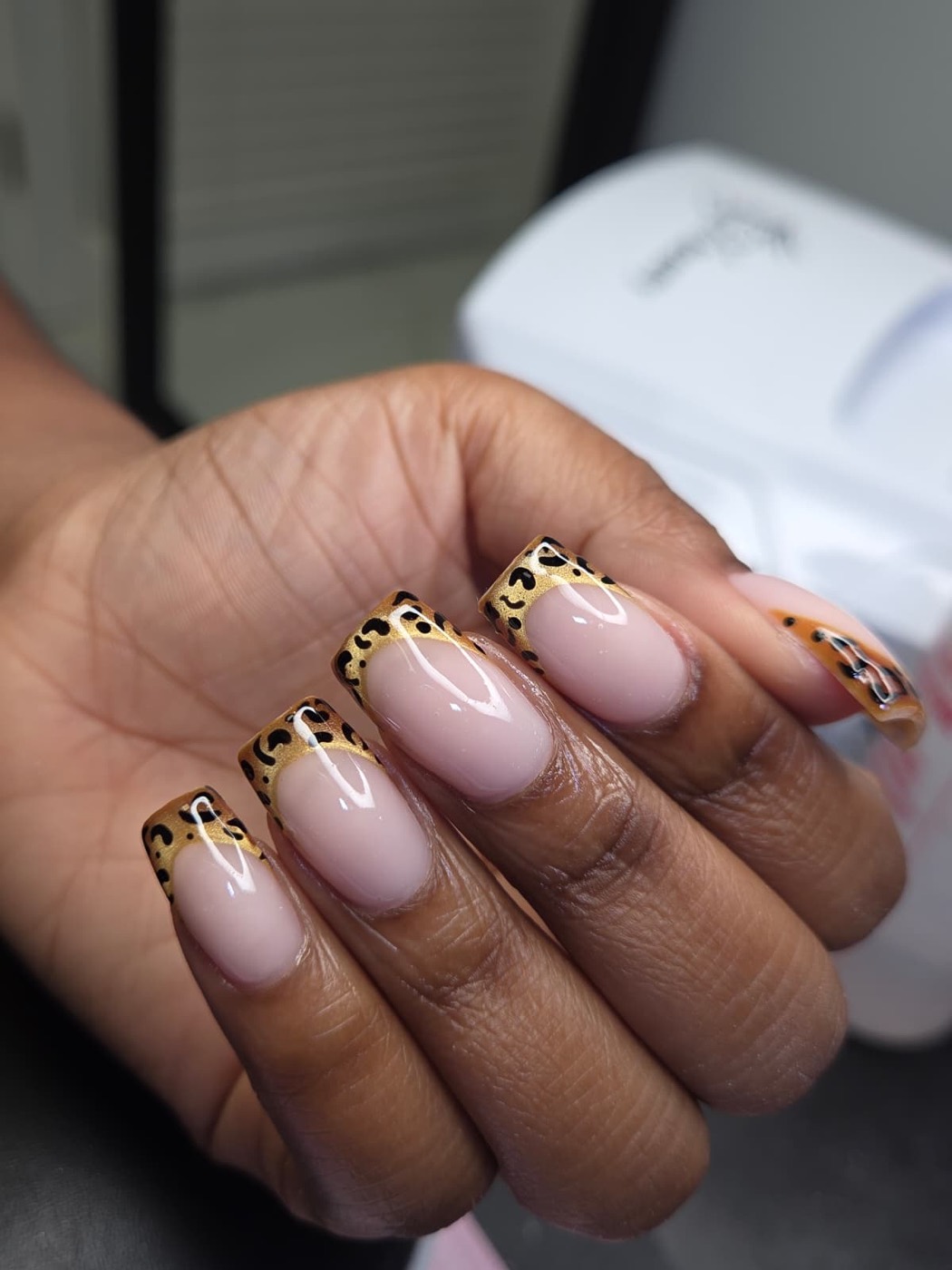 Square nails with gold and black leopard print French tips over a nude base
