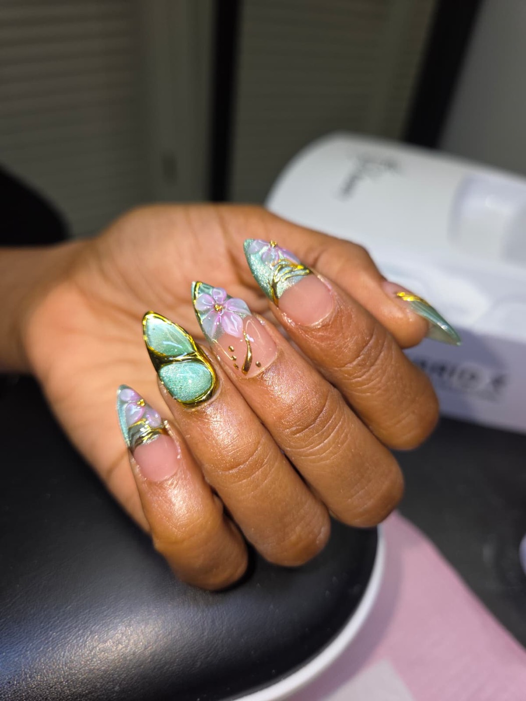 Mint green cat eye almond nails with 3D lilac flowers and gold trim