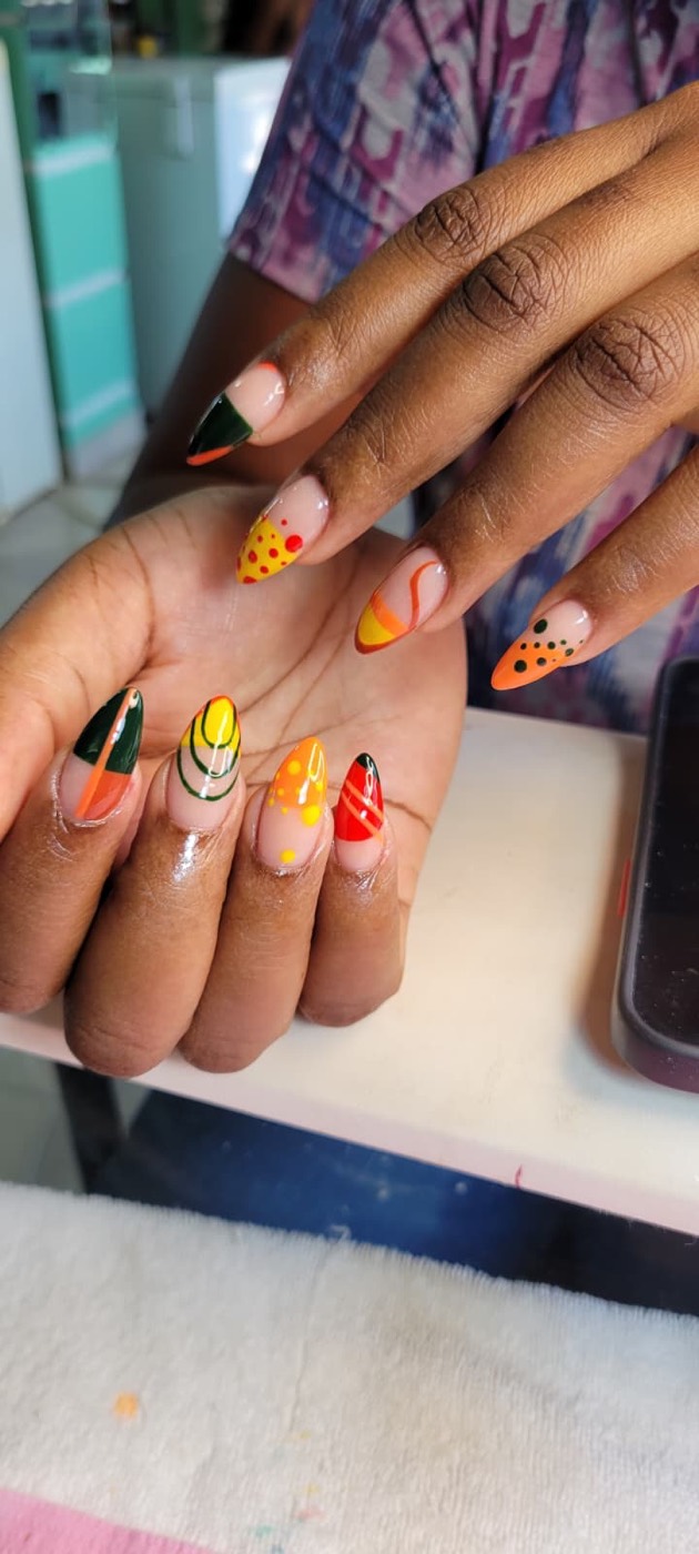 Stiletto nails with green, yellow, and orange abstract art — dots, swirls, and stripes