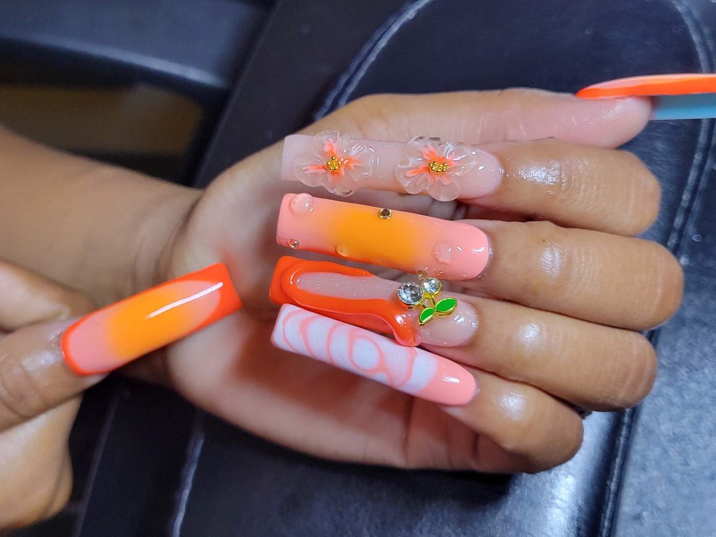 Extra long coffin nails in neon orange with 3D flowers, cherry charms, and marble accents