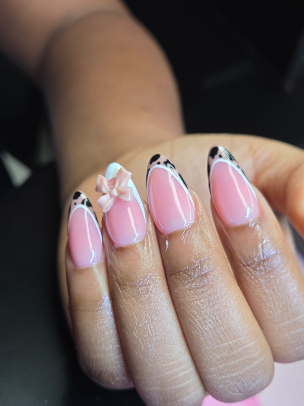 Pink almond nails with white French outlines, cow print tips, and a 3D bow accent